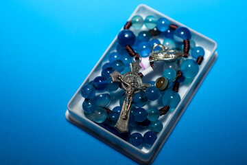 ​A rosary with bright blue natural stone beads and a silver crucifix rests in a small rectangular...