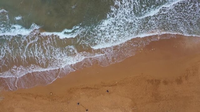 Aerial view of the foamy turquoise sea meeting the sandy beach creating a mesmerizing contrast of textures and tones, Gozo Island, Gozo, Malta.