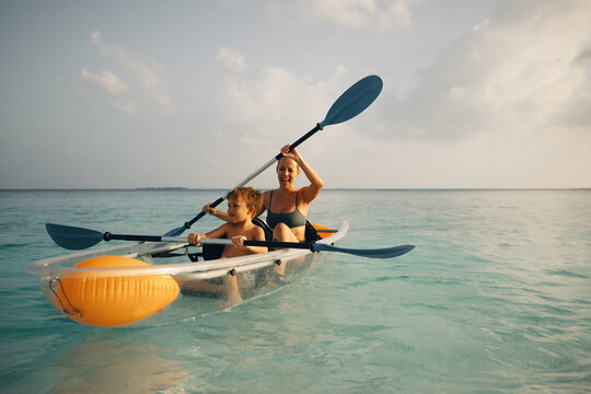 Woman and boy kayaking in clear canoe on a tranquil sea enjoying an outdoor adventure - Powered by Adobe