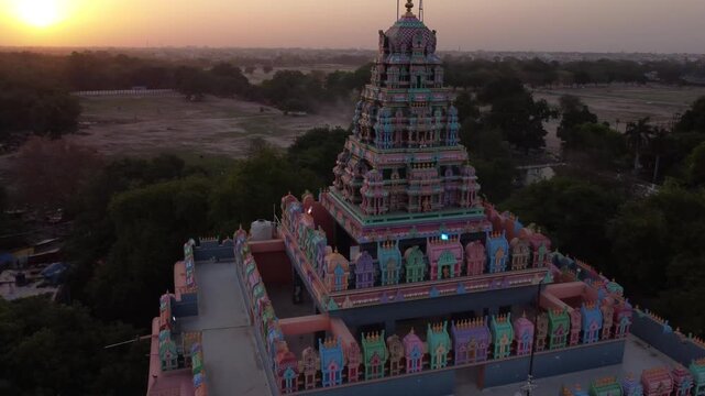 Aerial view of a tiered temple exhibiting vibrant pinks, blues, and greens, standing tall against a backdrop of trees and a soft sunset, Prayagraj, Uttar Pradesh, India.
