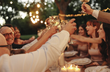 Celebration with friends toasting wine glasses outdoors under warm glowing lights