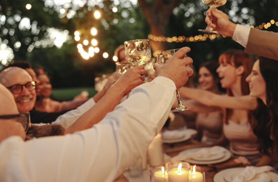 Celebration with friends toasting wine glasses outdoors under warm glowing lights - Powered by Adobe