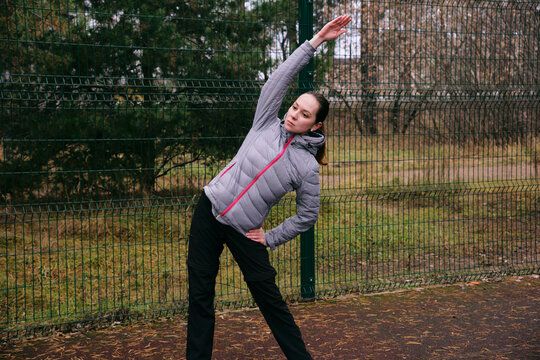 A young woman is doing a warm-up at the sports ground. The girl is doing side bends. Physical exercises and outdoor activity