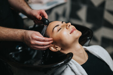 A client enjoys a soothing hair wash at a modern beauty salon. Warm water streams over her head as a stylist cleanses and relaxes, creating a calm, pampering spa experience.