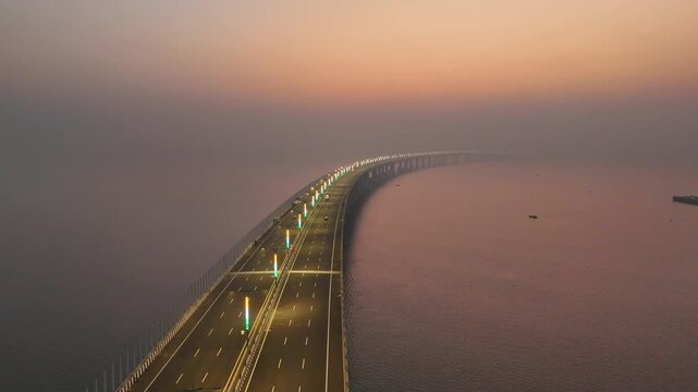 Aerial view of the Mumbai Trans Harbour Sea Link bridge extending over the water, illuminated by lights under a hazy sunrise sky, Mumbai, Maharashtra, India.