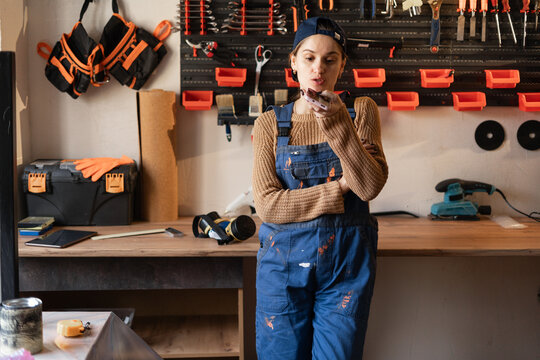 Carpenter woman talking on speakerphone, dictating voice message voice recognition in her small workshop