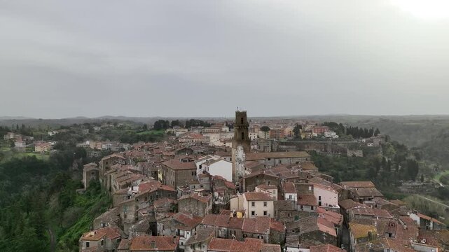 Aerial view of a townscape with close-packed buildings and a tall bell tower rising above the red-tiled roofs, Pienza, Tuscany, Italy.