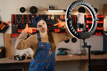 Craftsman or artisan blogger with ring light and smartphone streaming in workshop with assortment tools pointing with fingers on good smile. Blogging, industry and technology