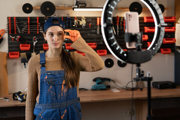 Craftsman or artisan blogger with ring light and smartphone streaming in workshop with assortment tools showing small size measure gesture. Blogging, industry and technology