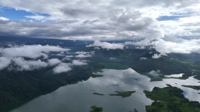 Aerial view of the tranquil Umiam Lake reflecting the sky, nestled amidst green hills and shrouded in soft, ethereal clouds, Shillong, Meghalaya, India.