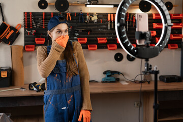 Shocked Craftsman or artisan blogger with ring light and smartphone streaming in workshop with assortment tools with bad news say omg. Face expression in wow. Blogging, industry and technology