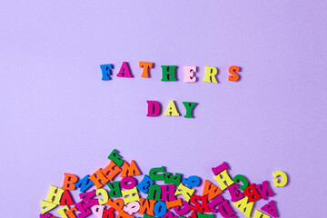 Child's toy letters spelling Fathers Day next to randomly lying letters on purple background. Concept photo. Flat lay design.
