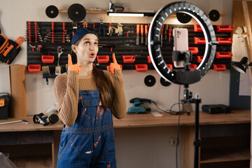 Craftsman or artisan blogger with ring light and smartphone streaming in workshop with assortment tools pointing fingers-up on advertisement space. Blogging, industry and technology