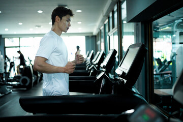Young fit handsome Asian man running on treadmill or running machine in modern fitness gym.