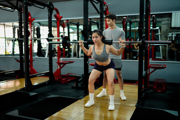 Professional fitness trainer guiding female athlete performing precise barbell squats in modern gym setting. Motivation and healthy lifestyle concept