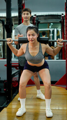 Professional fitness trainer guiding female athlete performing precise barbell squats in modern gym setting. Motivation and healthy lifestyle concept