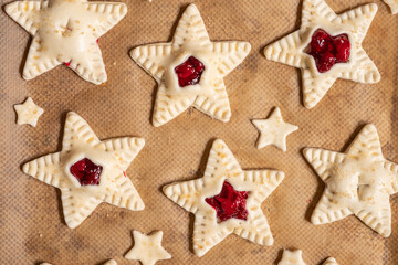 Delicious star-shaped cookies are ready for baking. The cookies are filled with red jam and placed on parchment paper. A rolling pin and a star-shaped cutter complete the scene.