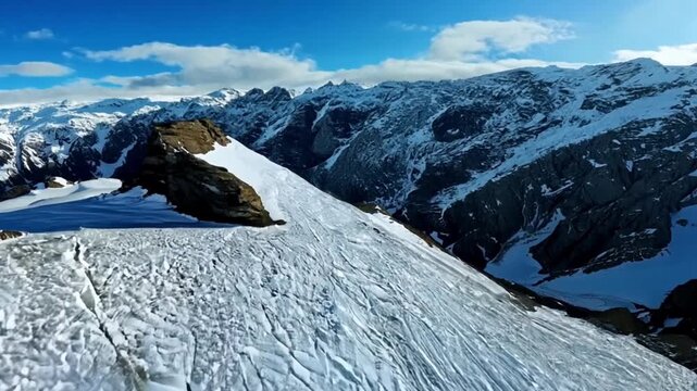 Aerial view of a snow covered mountain range with blue sky and some clouds in the background