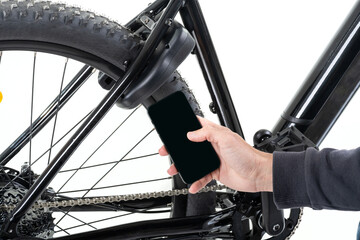 Unrecognizable male hand with a mobile phone, against the background of an electric bike with a smart lock device