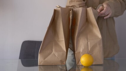 Hand taking fruits from grocery bag, calm domestic scene with fresh items on table, relaxed shopping moment reflecting simple healthy living. Woman sorts out food order, online shopping. 