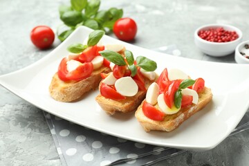 Tasty bruschettas with mozzarella cheese, tomatoes, basil and spices on grey textured table, closeup