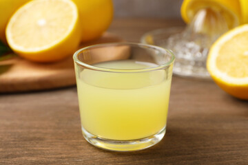 Lemon juice in glass and fresh lemons on wooden table, closeup