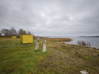 Couple of statues are standing in a field next to a body of water