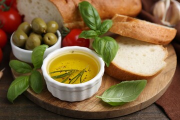 Tasty baguette served with oil, tomatoes, olives and basil on wooden table, closeup