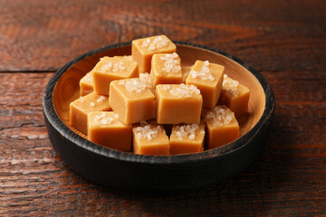 Tasty caramel candies with salt in bowl on wooden table, closeup