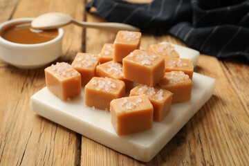 Tasty candies with salt and caramel sauce on wooden table, closeup