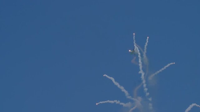 Military aircraft deploying multiple flares in sky during tactical maneuver