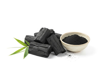 natural composition features several pieces of black charcoal chunks and a wooden bowl filled with fine black charcoal powder. A small wooden scoop holds more powder, and fresh green bamboo leaves add