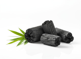 natural composition features several pieces of black charcoal chunks and a wooden bowl filled with fine black charcoal powder. A small wooden scoop holds more powder, and fresh green bamboo leaves add