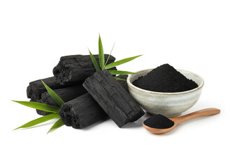 natural composition features several pieces of black charcoal chunks and a wooden bowl filled with fine black charcoal powder. A small wooden scoop holds more powder, and fresh green bamboo leaves add