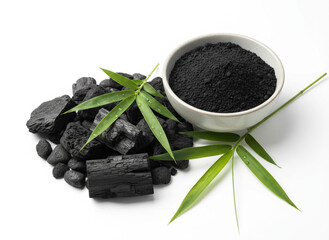 natural composition features several pieces of black charcoal chunks and a wooden bowl filled with fine black charcoal powder. A small wooden scoop holds more powder, and fresh green bamboo leaves add