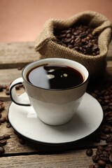 Aromatic coffee in cup and beans on wooden table against brown background, closeup
