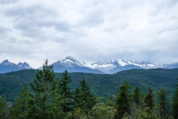 Obraz premium mountain with ice and snow at the top of the hill taken from the Tantalus Lookout, Squamish, British Columbia, Canada on a cloudy day with forest and trees