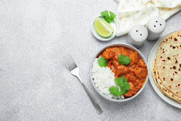 Delicious chicken tikka masala with rice, cilantro, lime and spices served on grey textured table, flat lay. Space for text