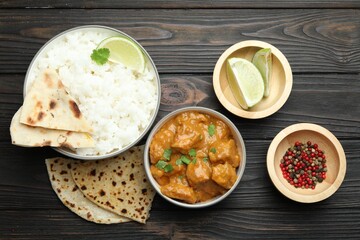 Delicious chicken tikka masala with rice, cilantro, lime, lavash and peppercorns on wooden table, flat lay