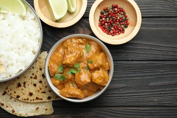 Delicious chicken tikka masala with rice, cilantro, lime, lavash and peppercorns on wooden table, flat lay. Space for text