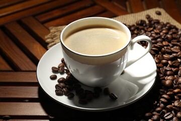 Aromatic coffee in cup and beans on wooden table, closeup