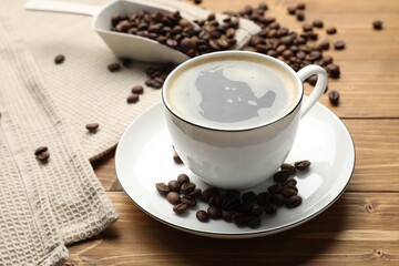 Aromatic coffee in cup and beans on wooden table, closeup