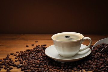 Aromatic coffee in cup and beans on wooden table against brown background, closeup. Space for text