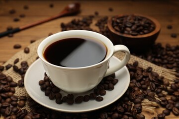 Aromatic coffee in cup and beans on wooden table, closeup