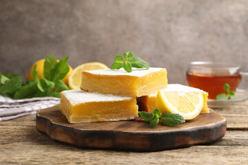 Tasty lemon bars with mint, fresh fruits and tea on wooden table, closeup