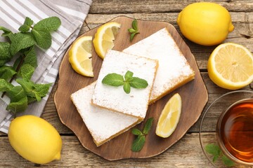 Tasty lemon bars with mint, fresh fruits and tea on wooden table, flat lay