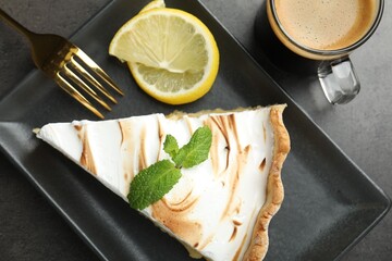 Slice of tasty lemon meringue tart with mint served on black table, flat lay