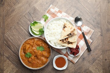 Delicious chicken tikka masala, rice, cilantro, lime, lavash and spices on wooden table, flat lay
