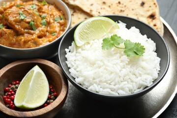 Delicious rice, lime, cilantro, chicken tikka masala and peppercorns on grey table, closeup
