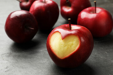 Red apple with carved heart and other fruits on black table, closeup